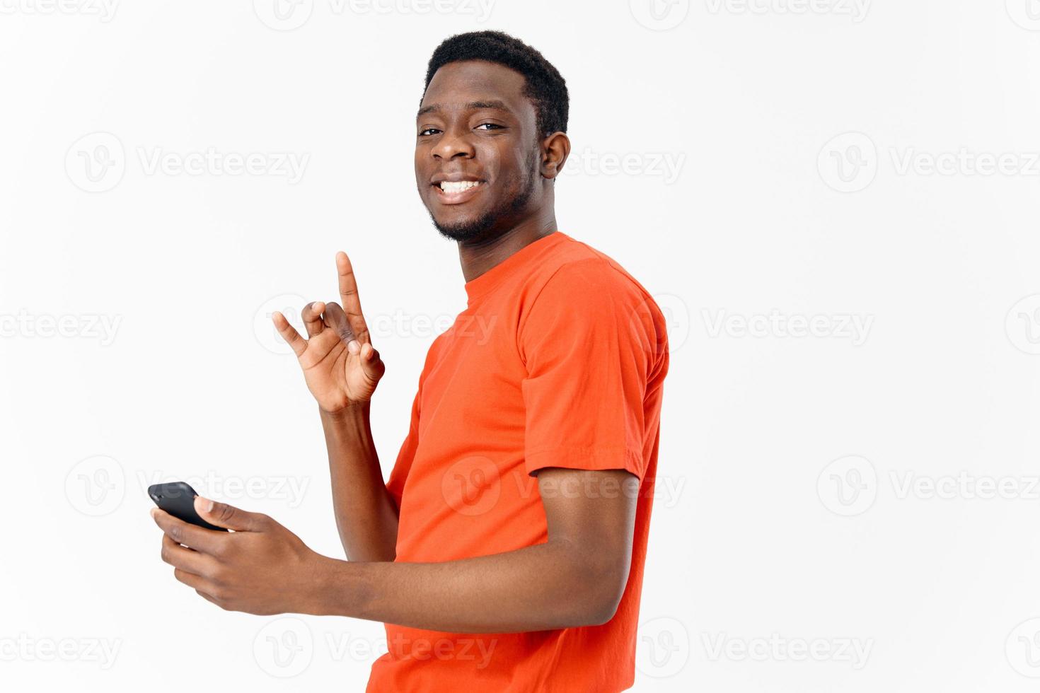 Lycklig kille av afrikansk utseende gestikulerar med hans händer och innehav en mobil telefon på en ljus bakgrund foto
