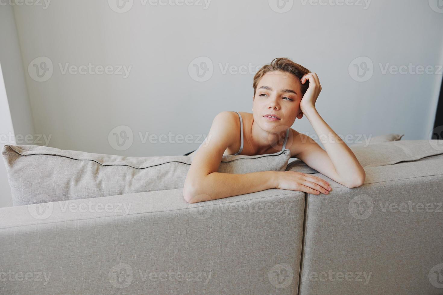 Lycklig kvinna leende liggande på Hem på de soffa avkopplande på en helgen på Hem med en kort frisyr hår utan filter på en vit bakgrund, fri kopia Plats foto