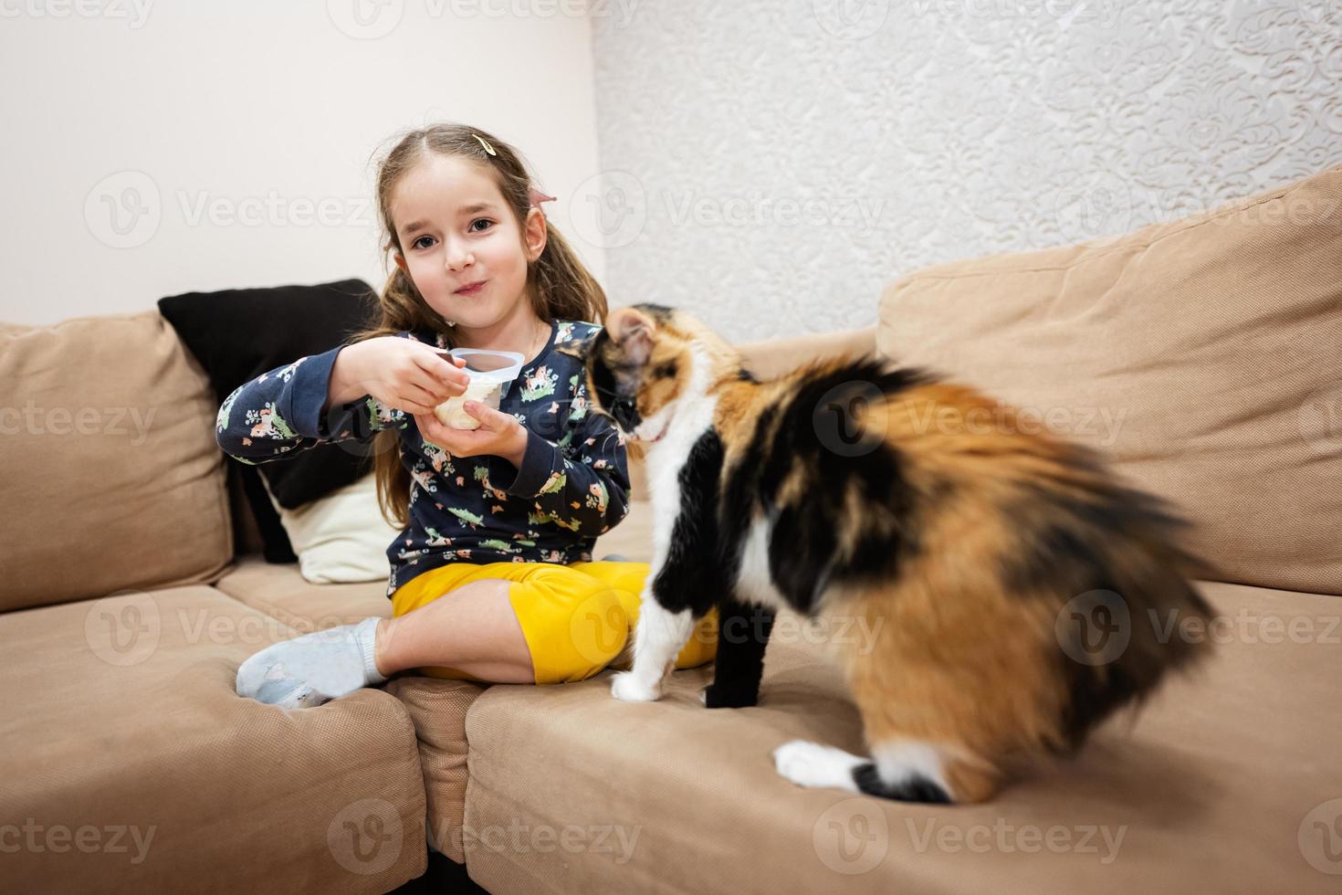 liten flicka utfodra de katt med yoghurt från en sked på Hem. foto