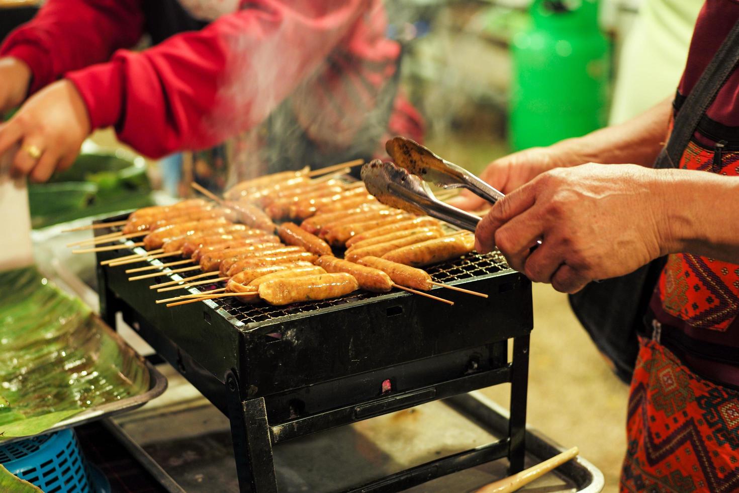 närbild rad köttkorvar på metallgrillen med rörelse suddiga händer foto