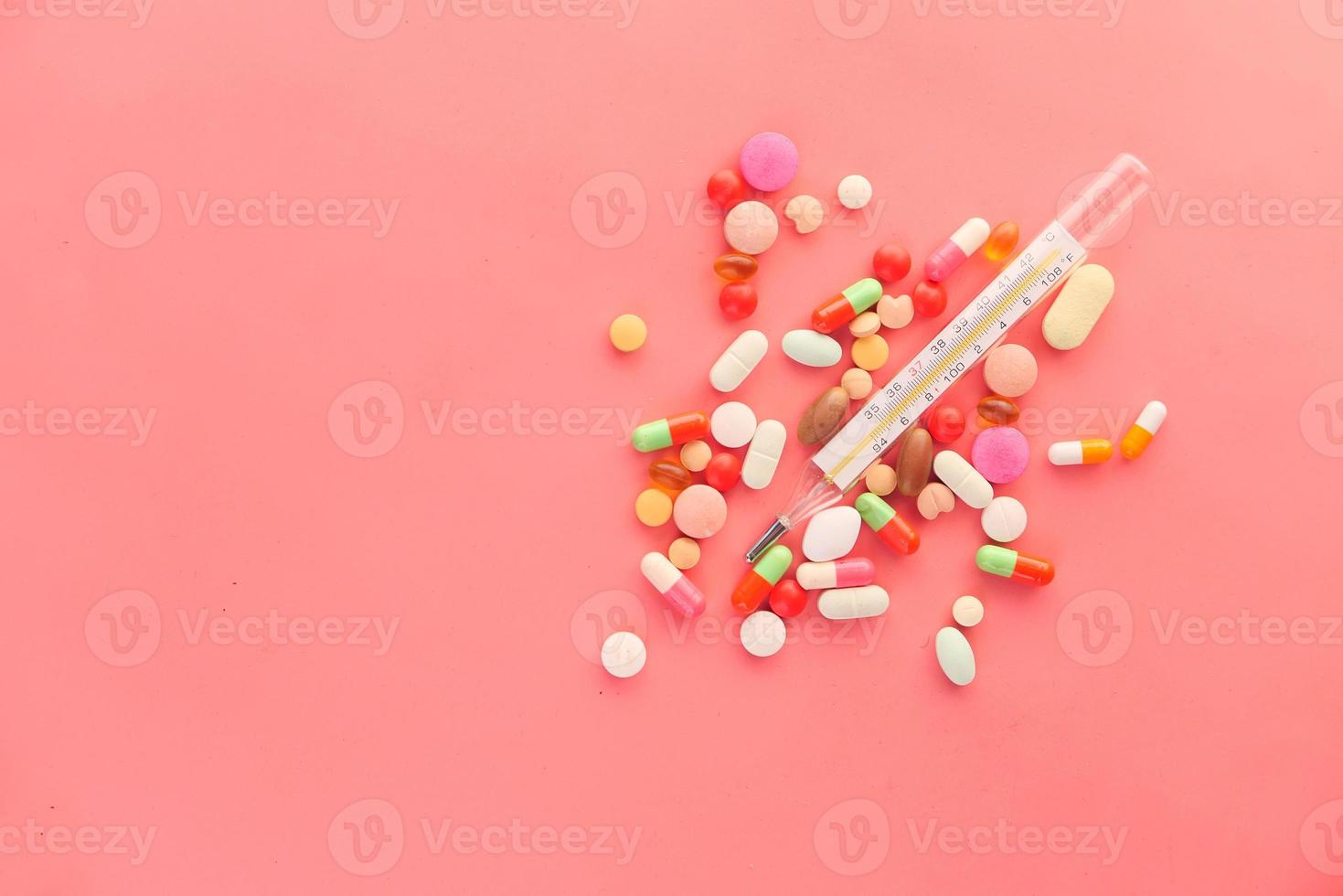 medicinsk termometer och piller på rosa bakgrund foto
