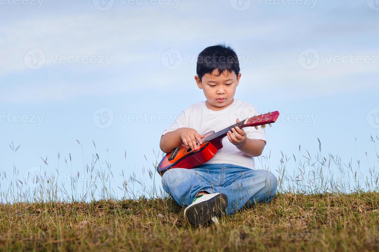 porträtt av asiatisk barn pojke spelar utomhus. Lycklig pojke med gitarr har roligt utomhus- foto