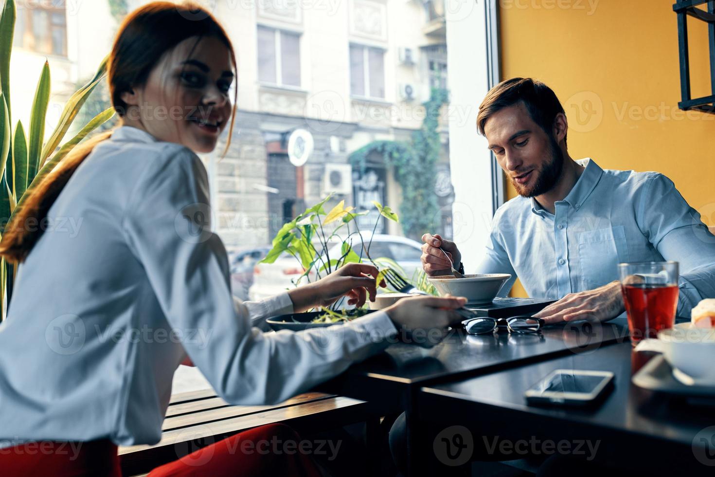 en kvinna i en ljus skjorta och en företag man ha lunch på en tabell i en Kafé utsökt mat drycker anställda foto