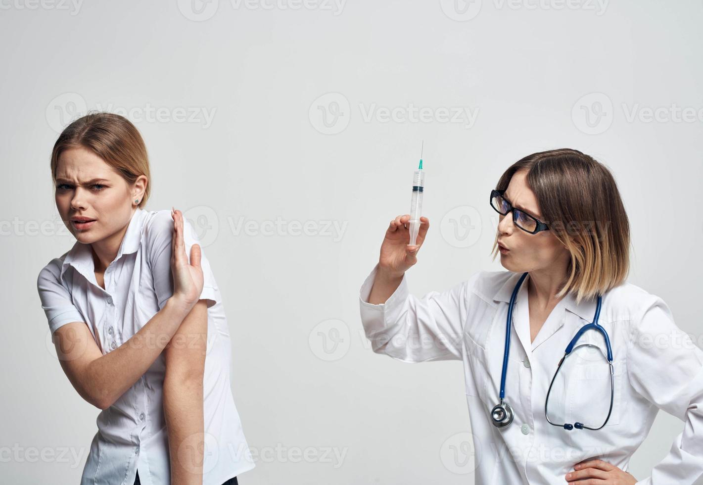 en kvinna innehar en spruta i henne hand och en kvinna patient i en vit t-shirt är skrämd modell foto