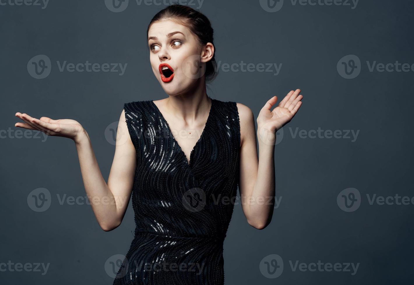 en kvinna i en svart klänning gester med henne händer överraskning glädje känslor. foto