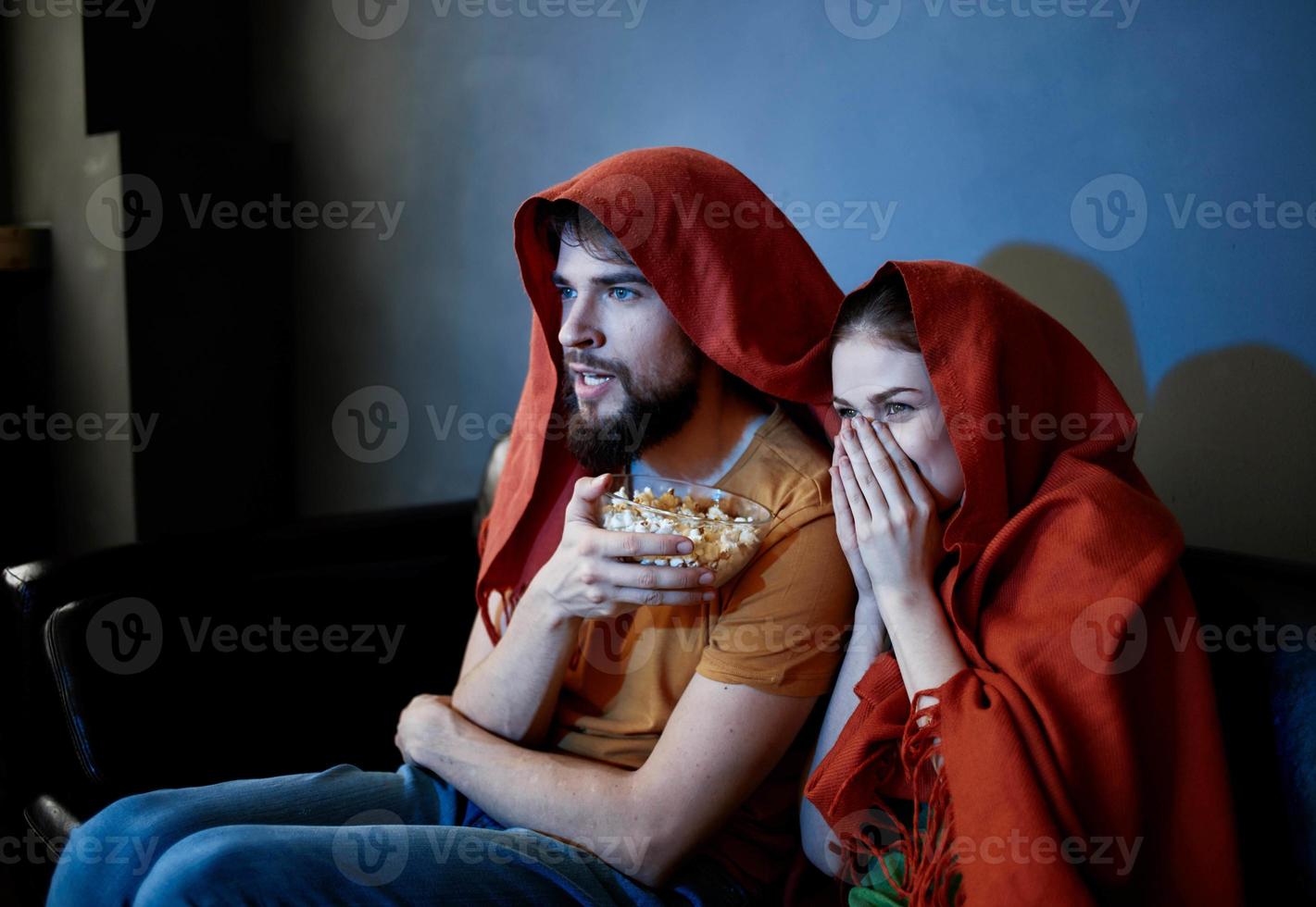 en man och en kvinna med en röd pläd på deras huvuden är Sammanträde på de soffa i främre av de TV inomhus foto