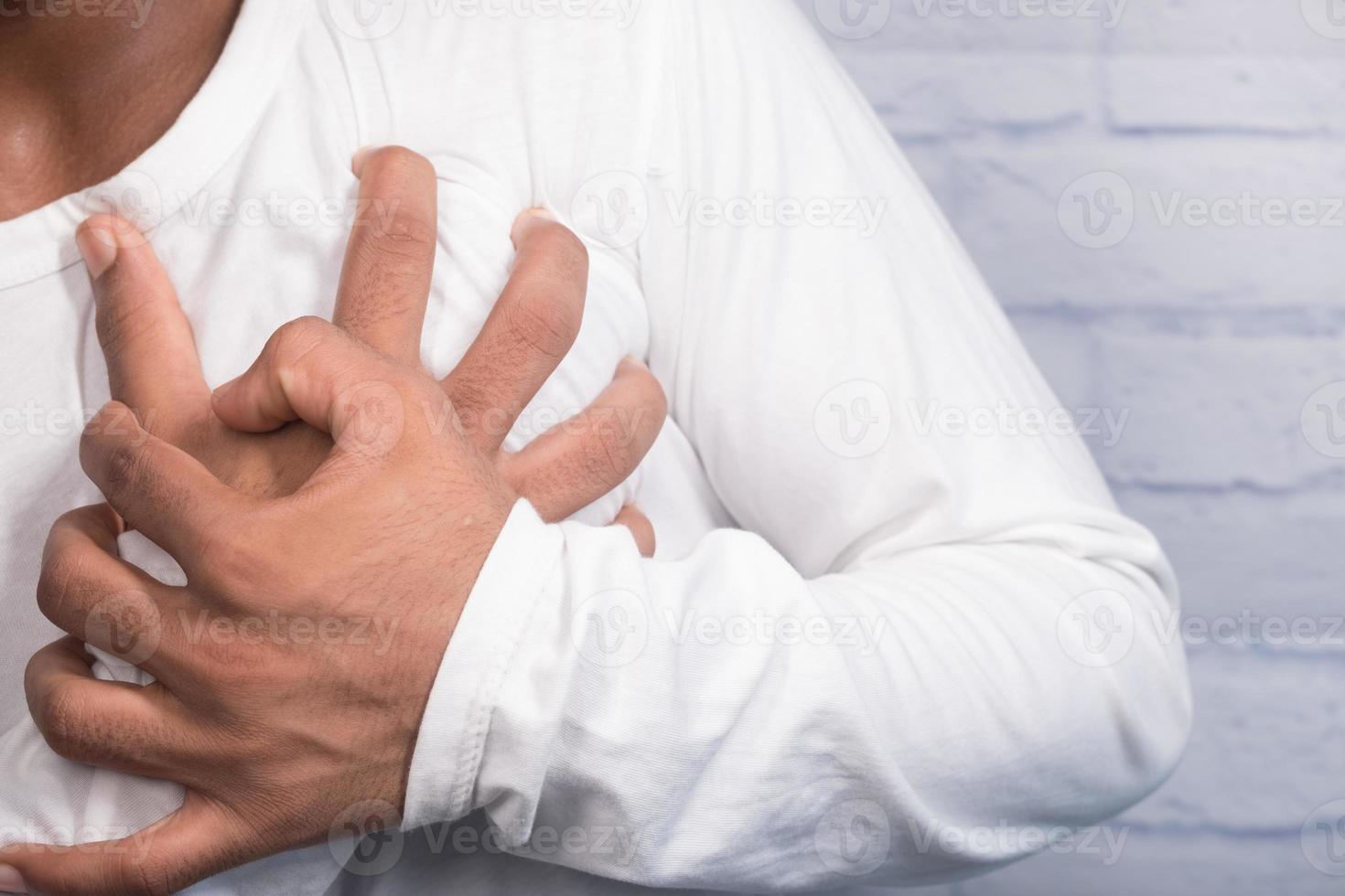 ung man lider av smärta i hjärtat och håller bröstet med handen foto