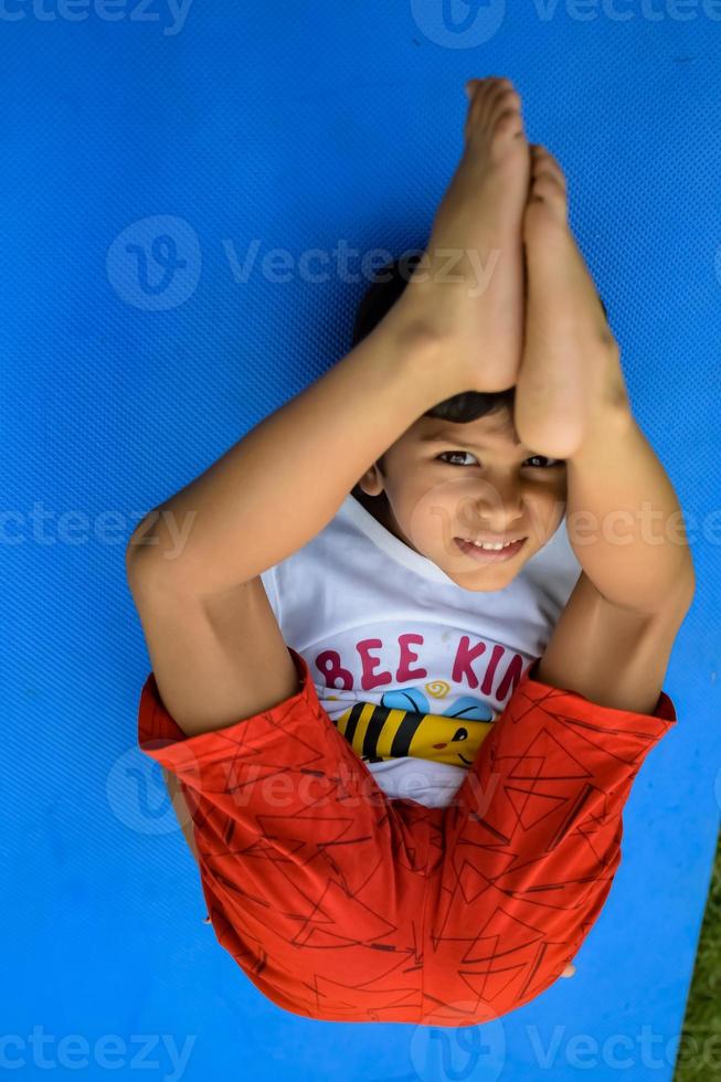 asiatisk smart unge håller på med yoga utgör i de samhälle parkera utomhus, barns yoga utgör. de liten pojke håller på med yoga träning. foto