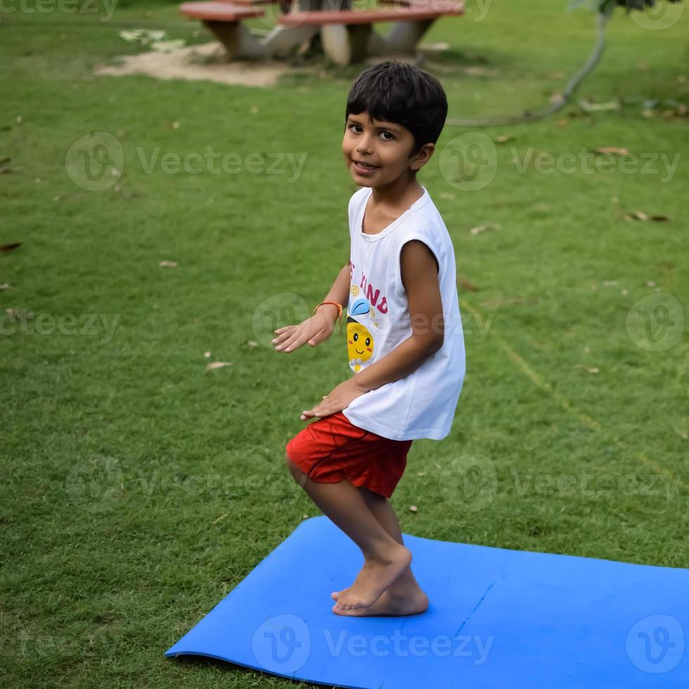 asiatisk smart unge håller på med yoga utgör i de samhälle parkera utomhus, barns yoga utgör. de liten pojke håller på med yoga träning. foto