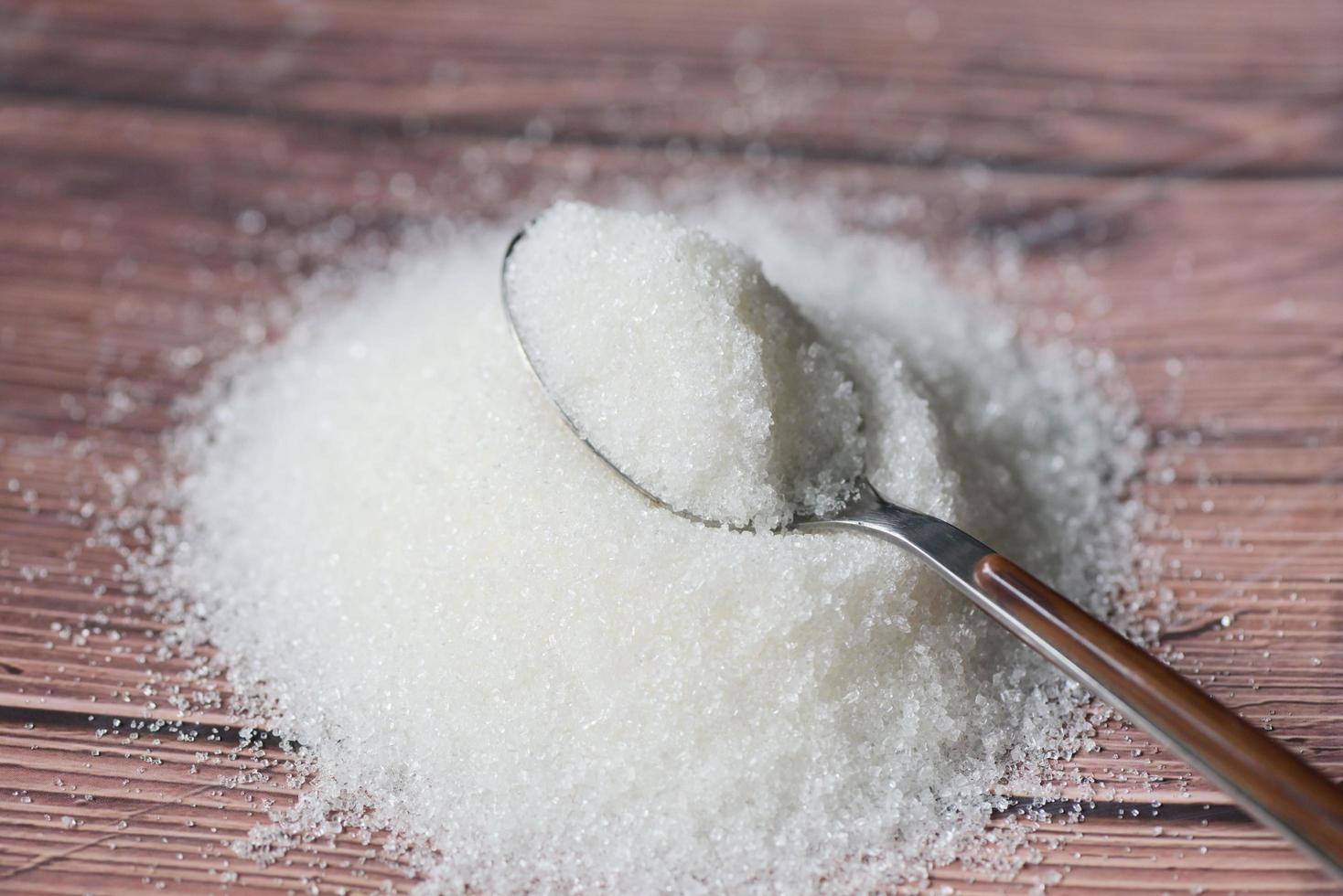 socker på sked och trä- bakgrund, vit socker för mat och sötsaker efterrätt godis högen av ljuv socker kristallin granulerad foto