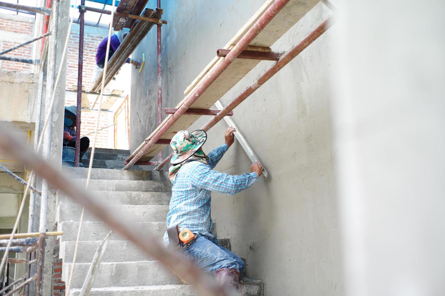 grupp arbetare står på stålställningen och bygger en putsad cementvägg i huset under konstruktion foto