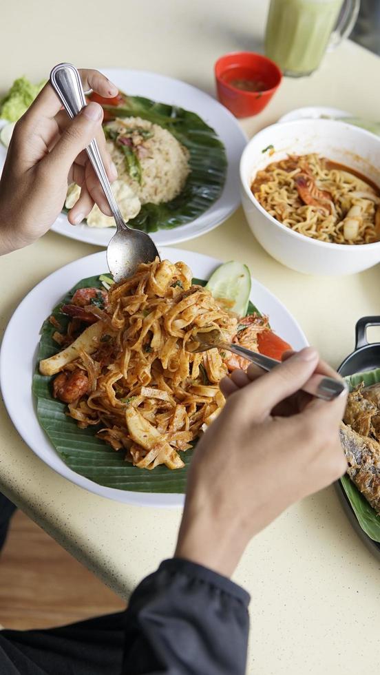 hand äter gest kryddad Vispa friterad nudel med ris och vegetabiliska på tabell foto