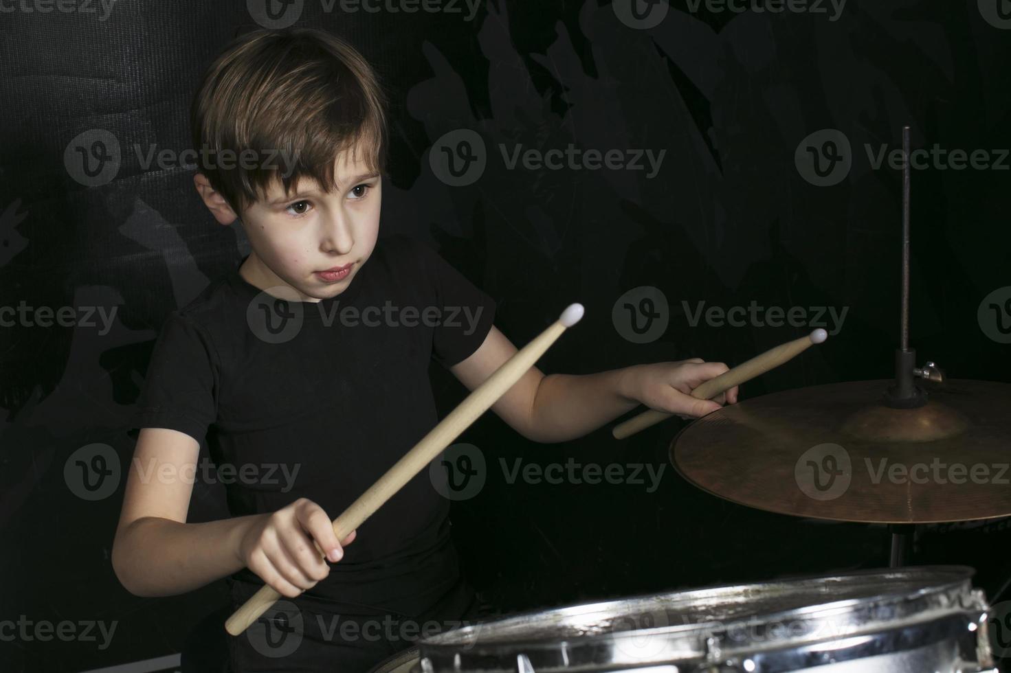 de barn Bakom de trumma. en pojke med trumpinnar Bakom en trumma utrustning. foto