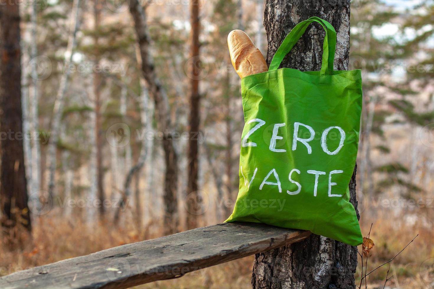 textil- grön väska med de inskrift noll avfall på en bakgrund av natur. franska bröd i en väska. selektiv fokus. suddigt träd och höst gräs på de bakgrund. foto