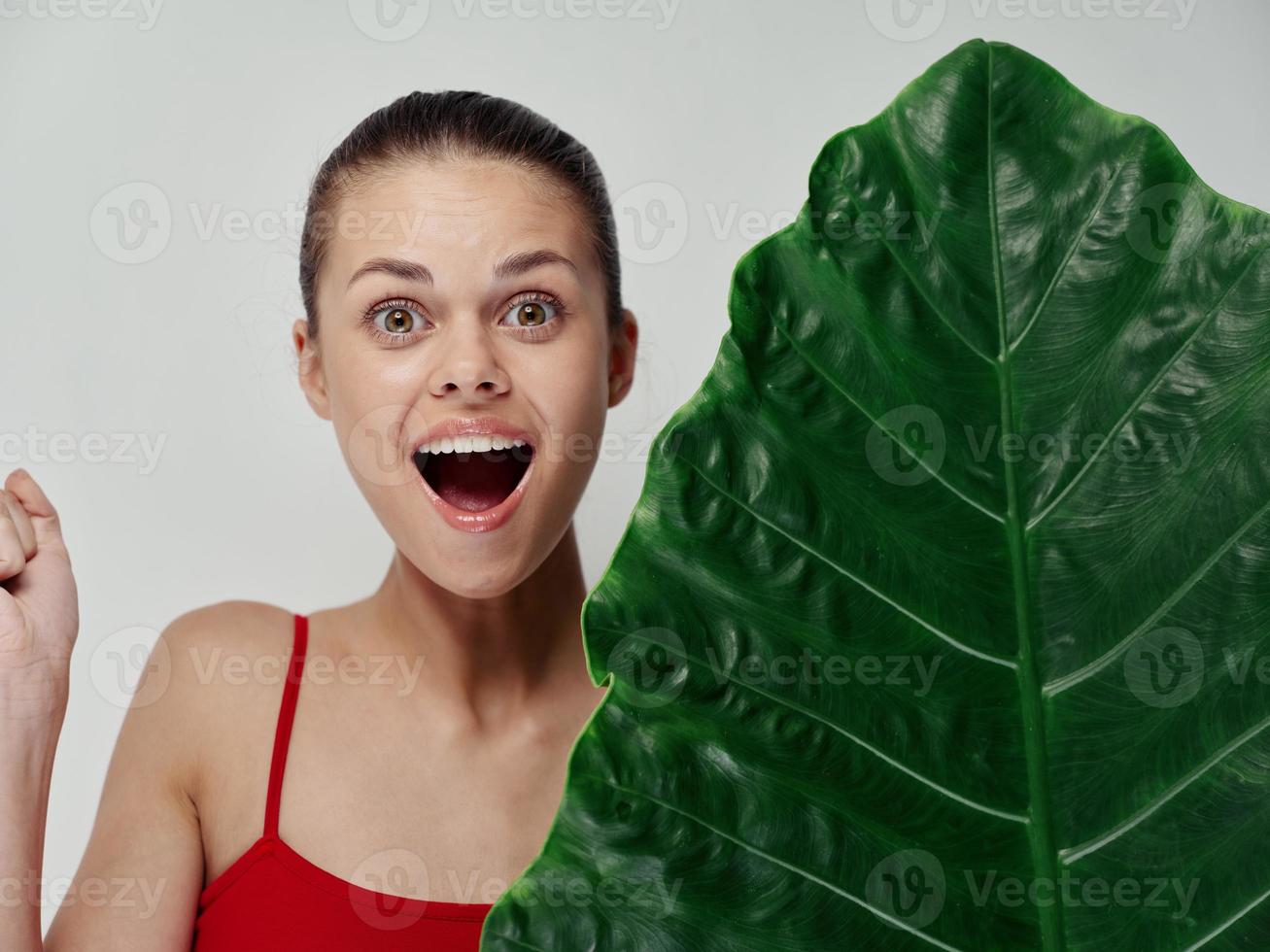 överraskad kvinna med öppen mun och grön blad handflatan ljus bakgrund foto