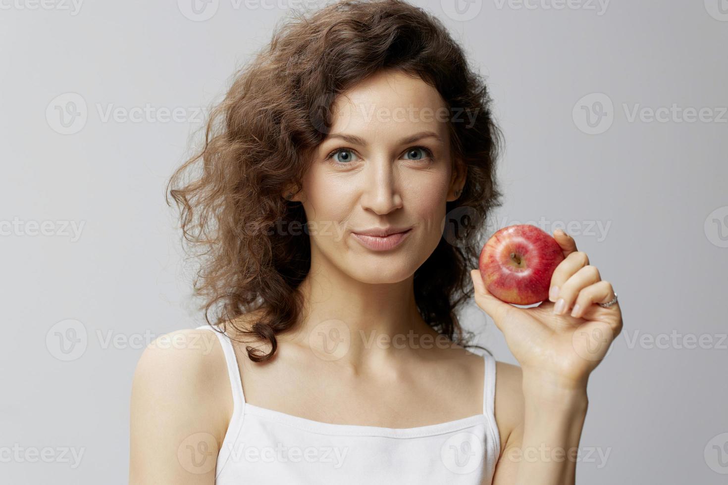 leende härlig söt lockigt skön kvinna i grundläggande vit t-shirt drar äpple njut av friska mat Framställ isolerat på över vit bakgrund. naturlig miljövänlig Produkter begrepp. kopia Plats foto