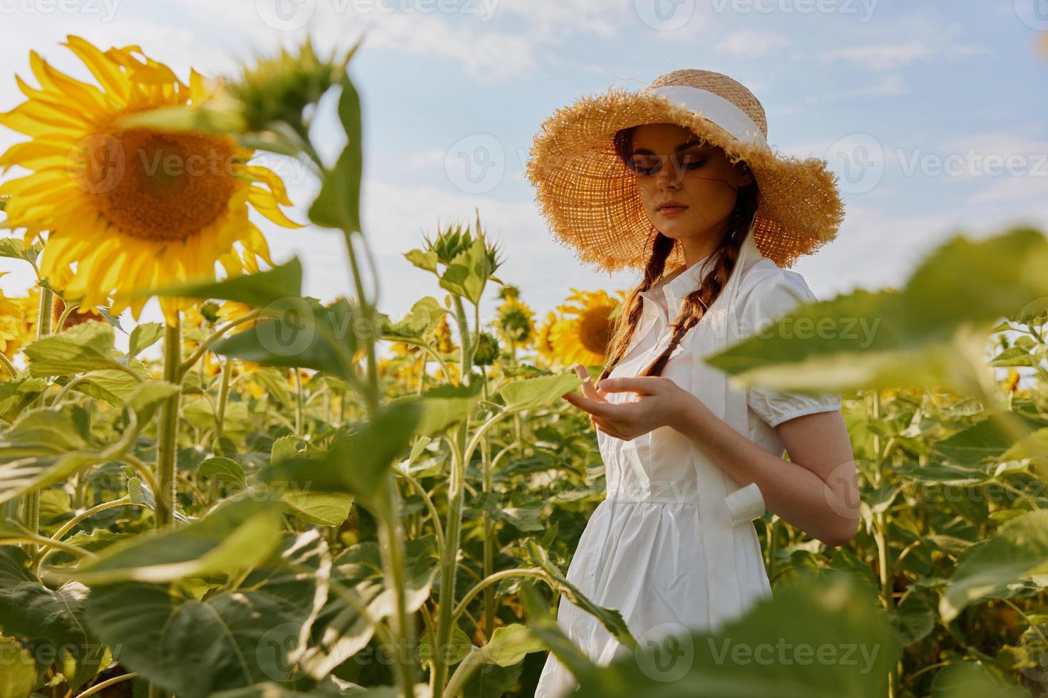kvinna med pigtails i en sugrör hatt i en vit klänning en fält av solrosor lantbruk oförändrad foto