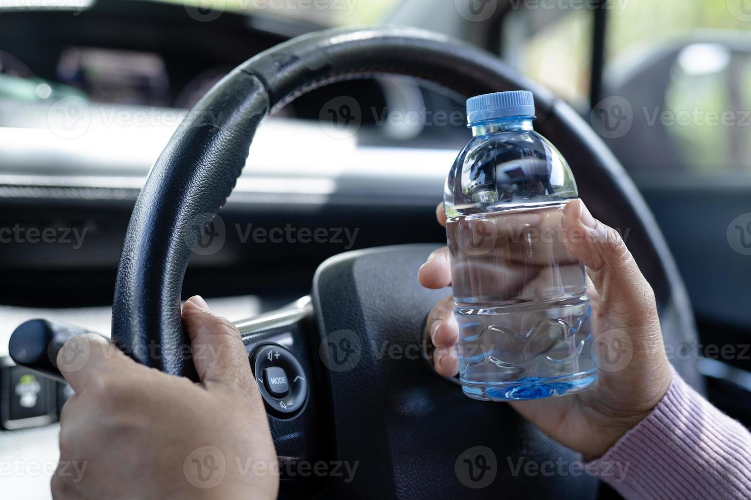 asiatisk kvinna förare håller flaska för att dricka vatten medan du kör bil. varmvattenflaska i plast orsakar brand. foto