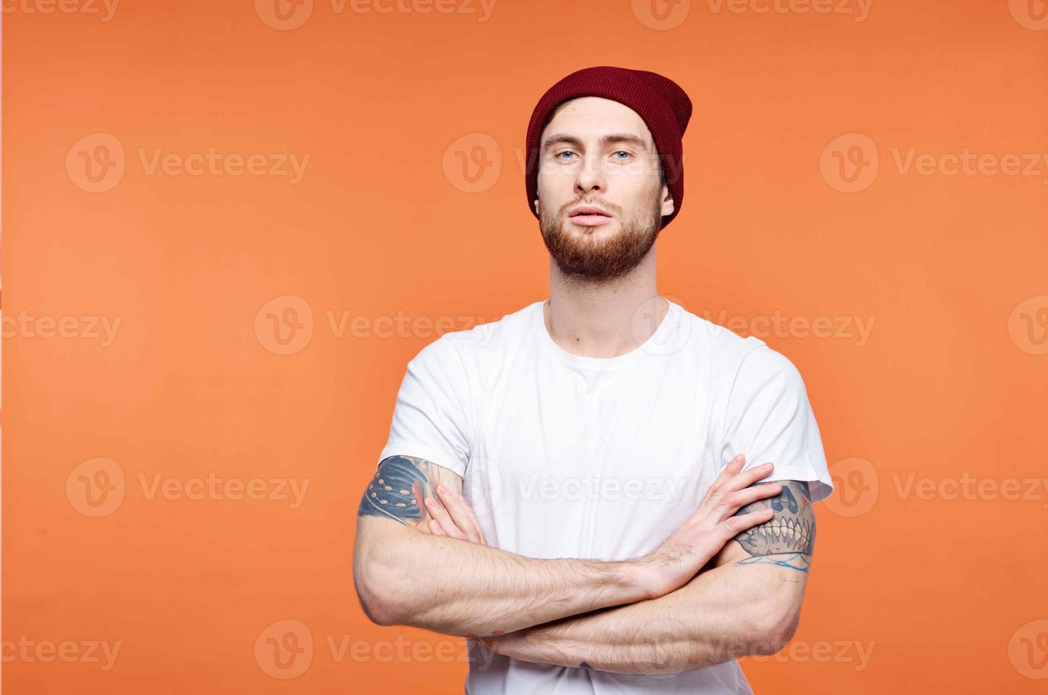 man i en vit t-shirt och en hatt tatuering på hans vapen orange bakgrund foto