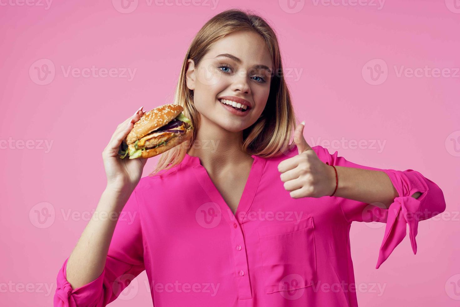 glad blond i en rosa skjorta hamburgare snabb mat mellanmål foto