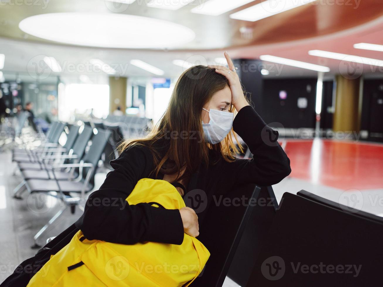 trött kvinna Sammanträde på de flygplats gul ryggsäck sida blick foto