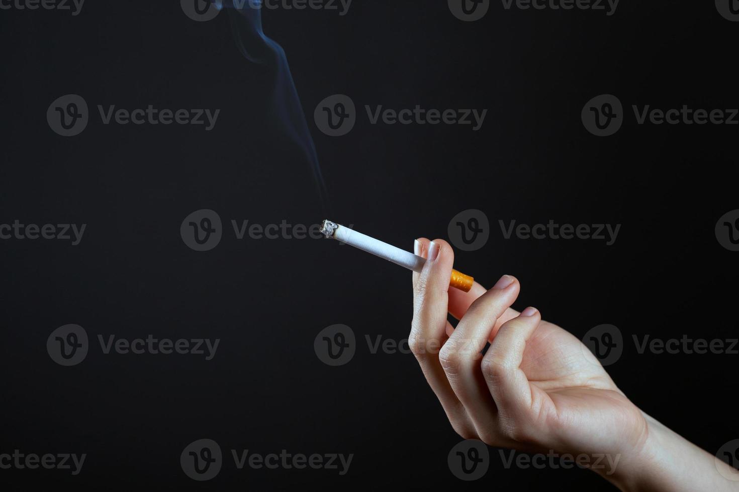 kvinnlig hand som håller en rökande cigarett på en mörk bakgrund med kopieringsutrymme foto