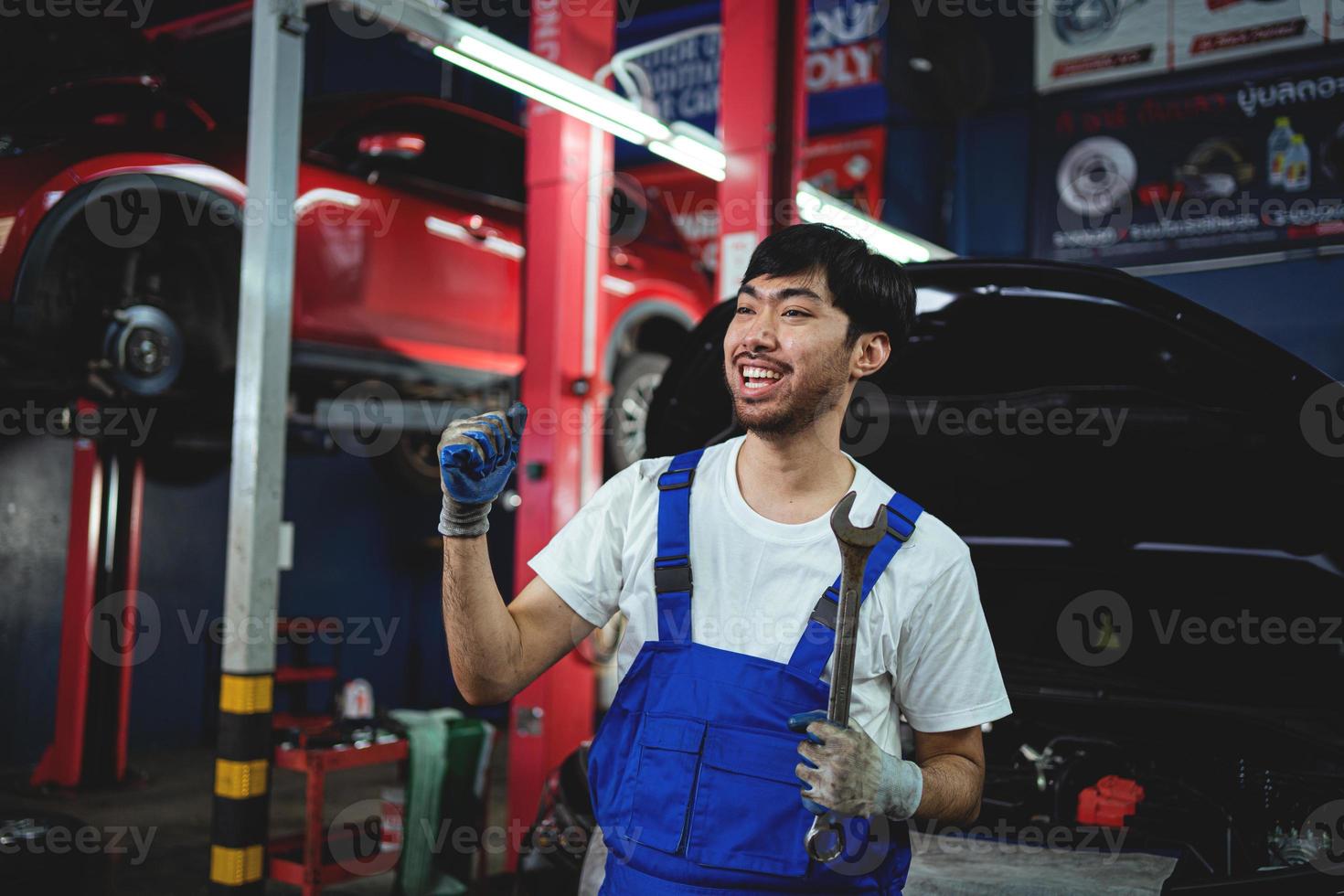 porträtt av leende asiatisk manlig reparatör innehav benen i kors rycka på garage professionell reparera och underhåll. bil inspektion service foto