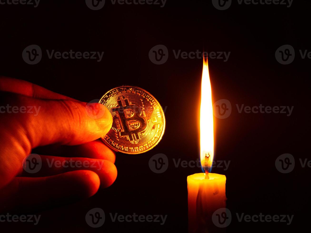 guld bitcoin mynt i handen i det varma ljuset av ett ljus på en mörk bakgrund foto