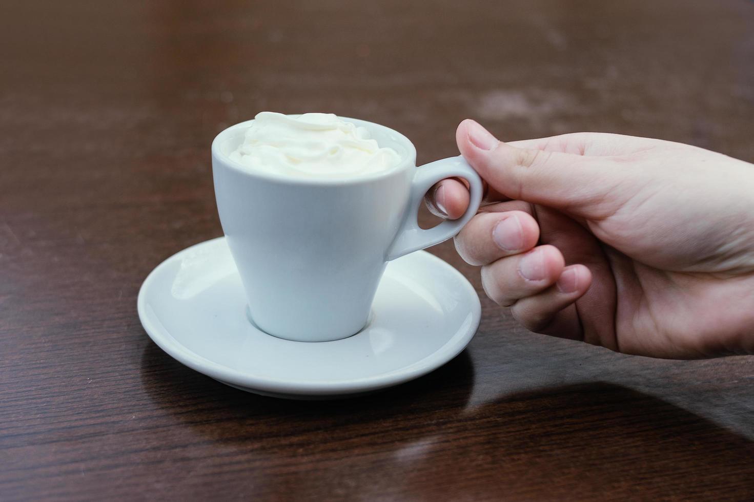 ovanifrån perspektiv av kaffe på ett bord. vit kaffekopp på brun blank bakgrund. kaffe med söt grädde. foto