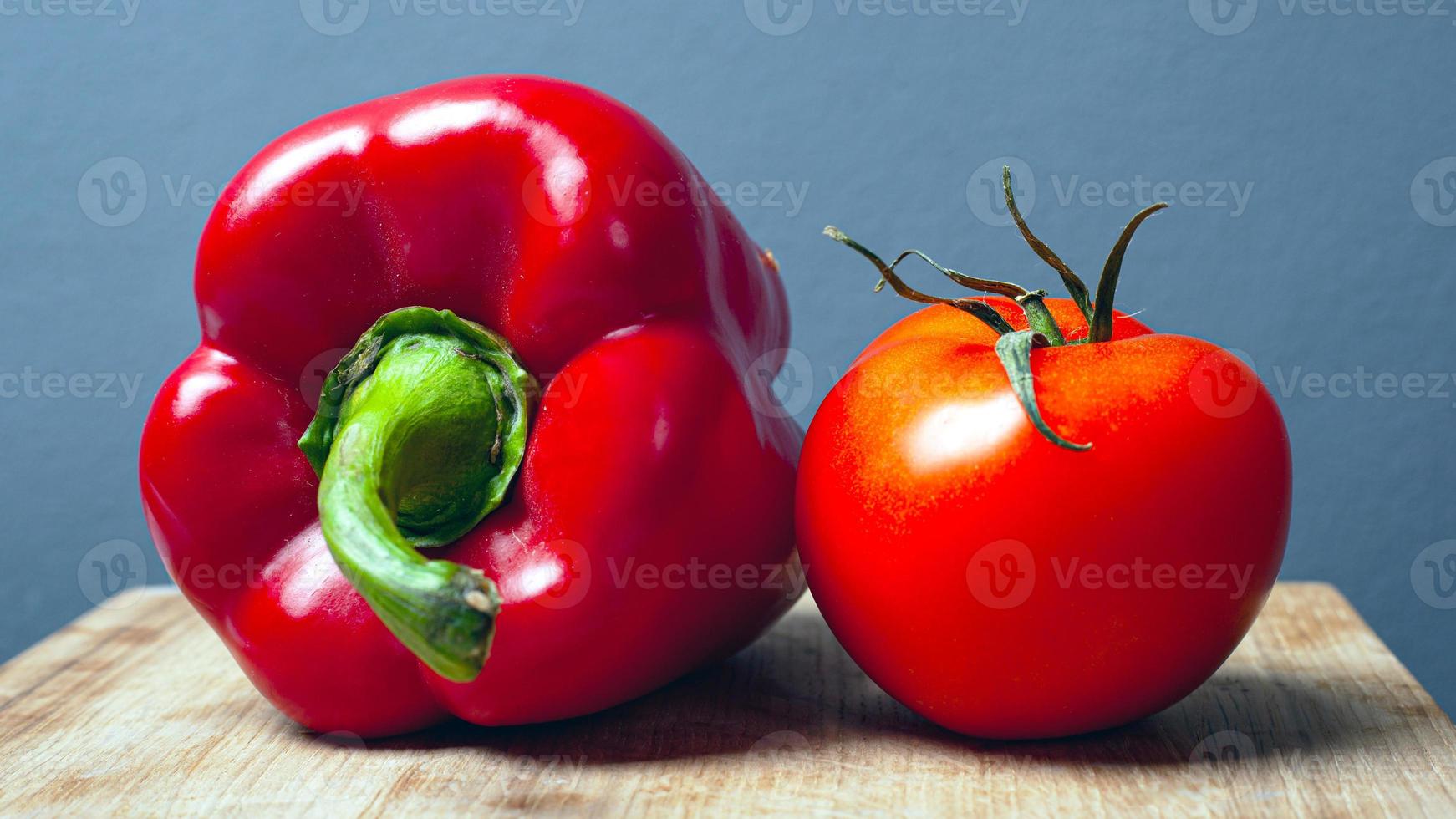 tomat och röd söt paprikapeppar på en träplatta på en grå bakgrund foto