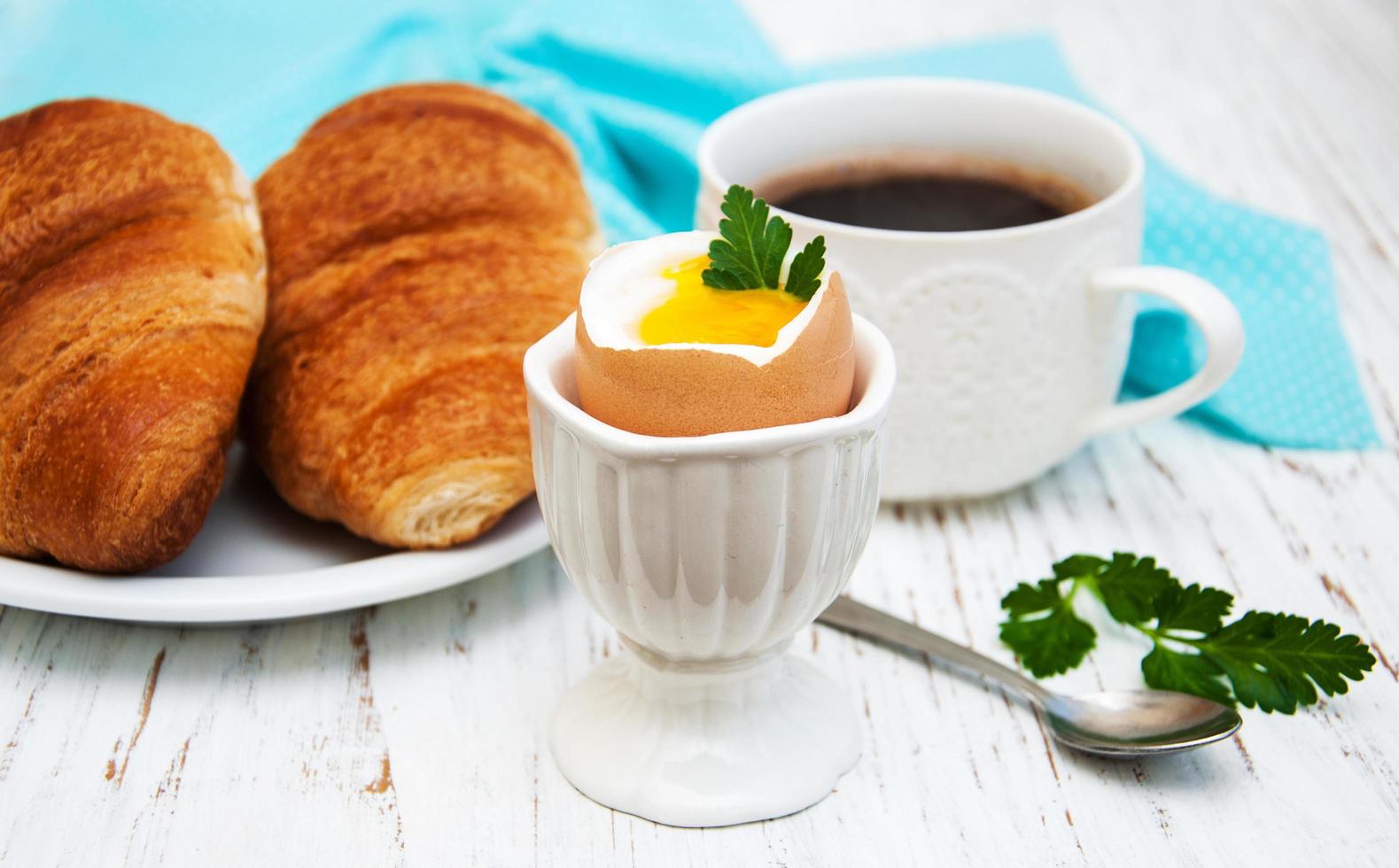 croissant, kokt ägg och kaffe på ett gammalt träbord foto