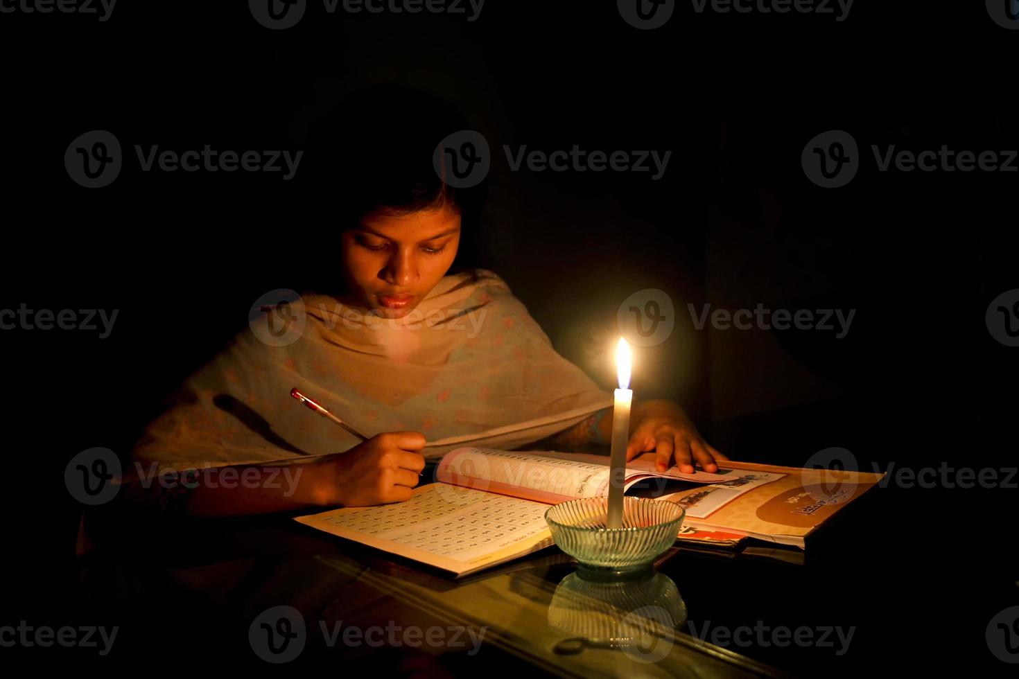 en ung flicka studerar på Hem med levande ljus efter elektricitet ladda shedding på dhaka stad. foto