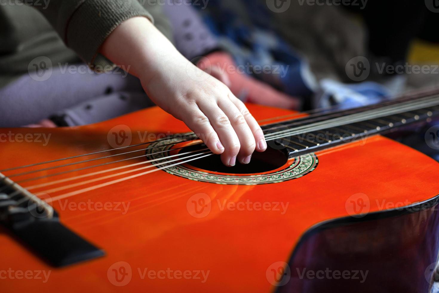 barns hand drar strängarna på en orange akustisk gitarr foto