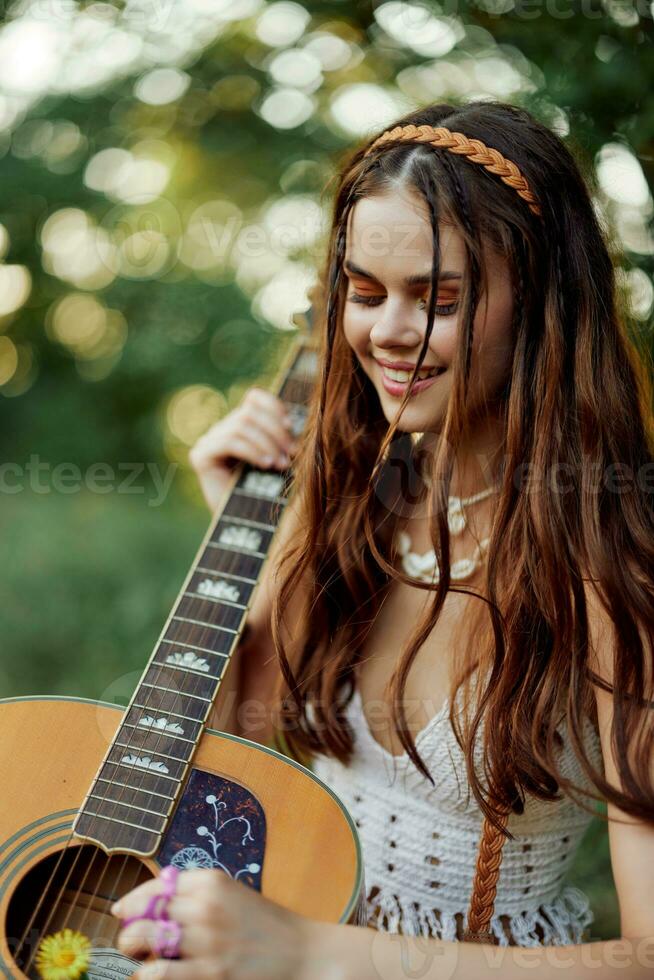 Lycklig hippie kvinna med en gitarr avkopplande i natur Sammanträde på en pläd leende och njuter de se. livsstil i harmoni med natur och själv foto