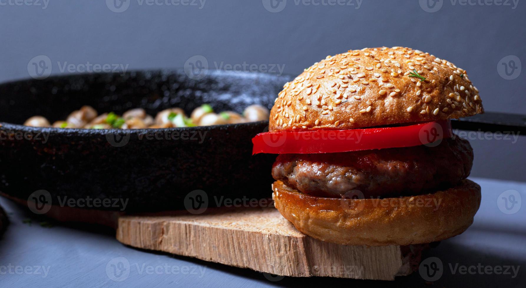 hamburgare med en saftig kotlett, mjuk bulle och champignonsvamp i en gjutjärnspanna foto