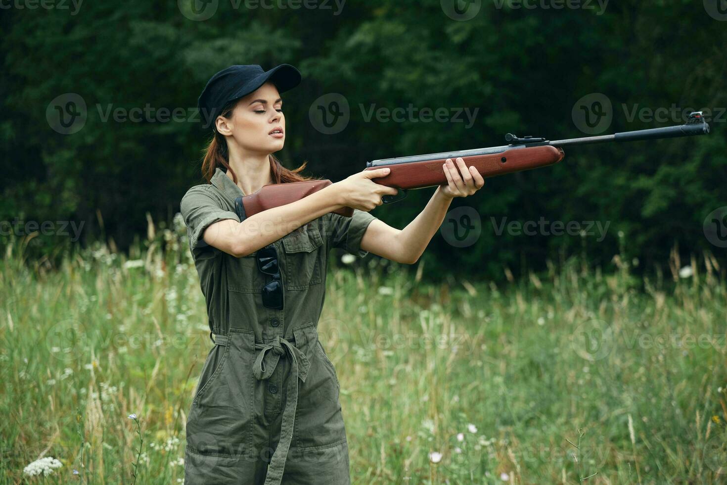 kvinna på utomhus- innehav en vapen i främre av honom jakt sida visningar grön löv grön foto