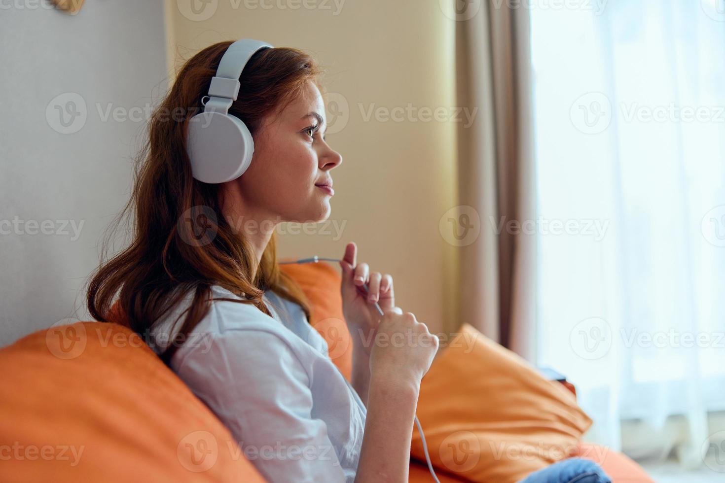 glad kvinna lyssnande till musik med hörlurar på de orange soffa teknik foto