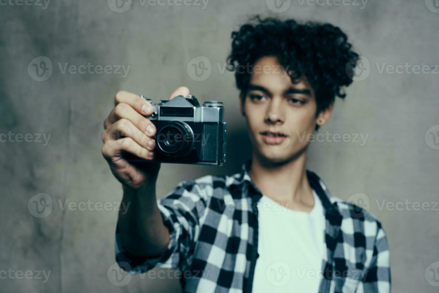 ung man med en kamera i hand och i en pläd t-shirt på en grå bakgrund inomhus fotograf foto