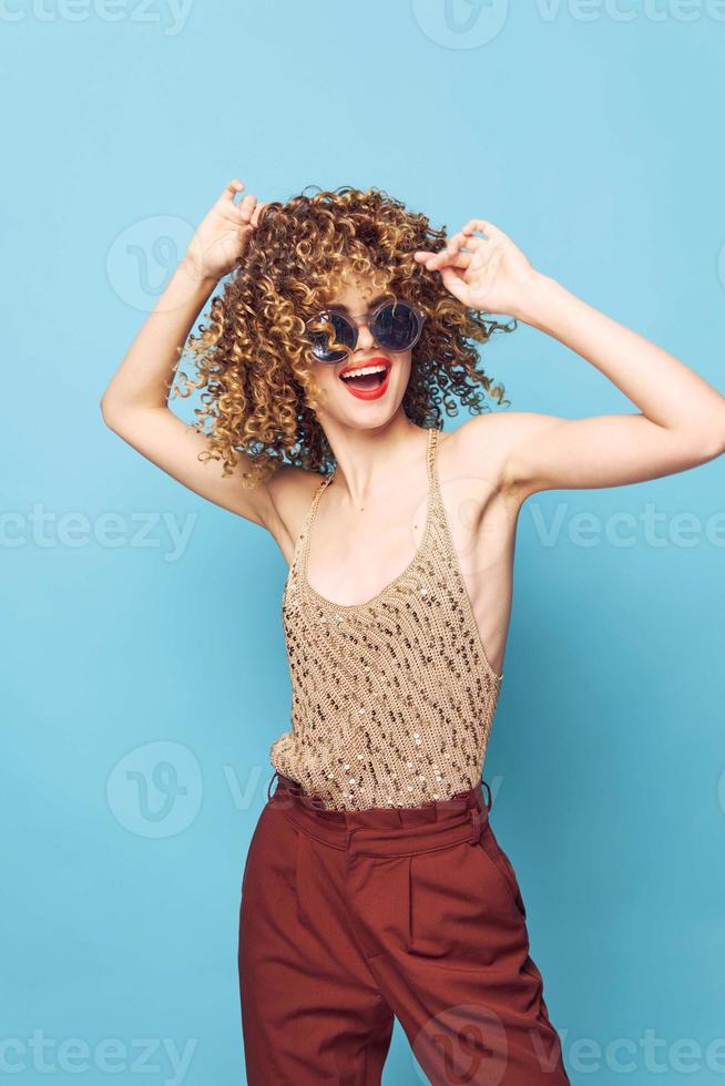 attraktiv kvinna lockigt hår roligt leende röd mun blå bakgrund röd byxor foto