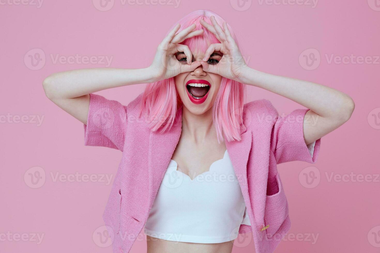 ung positiv kvinna gester med hans händer med en rosa jacka rosa bakgrund oförändrad foto
