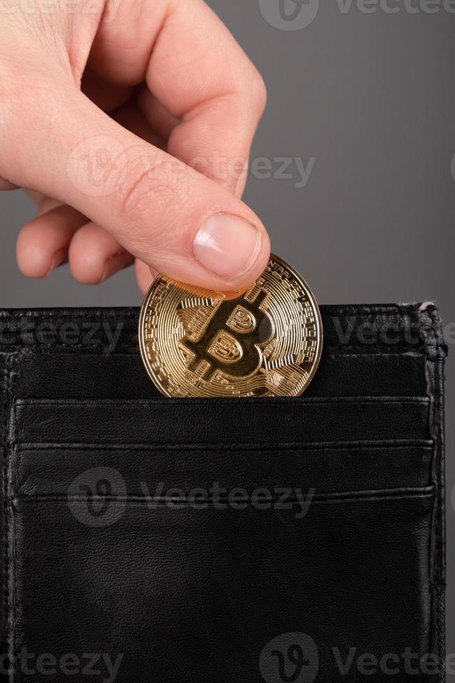 handen lägger ett bitcoin-mynt i plånboken foto