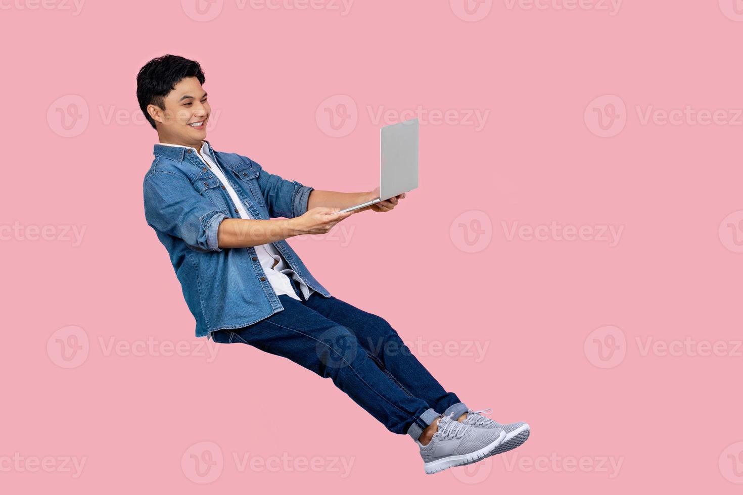 ung asiatisk affärsman innehav bärbar dator dator flytande i de luft isolerat på rosa bakgrund foto