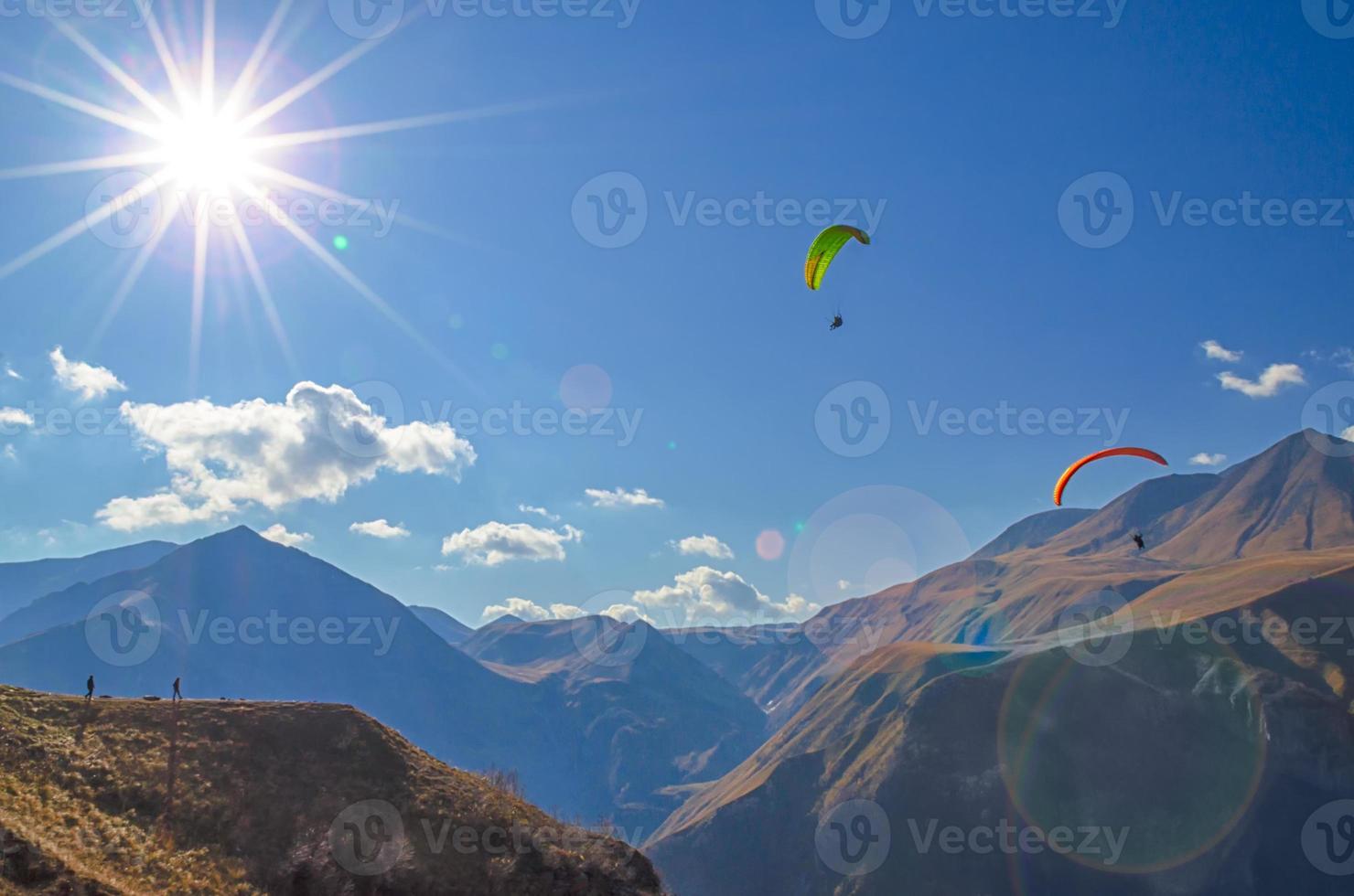 skärmflygare och turister på berg med solbländning foto