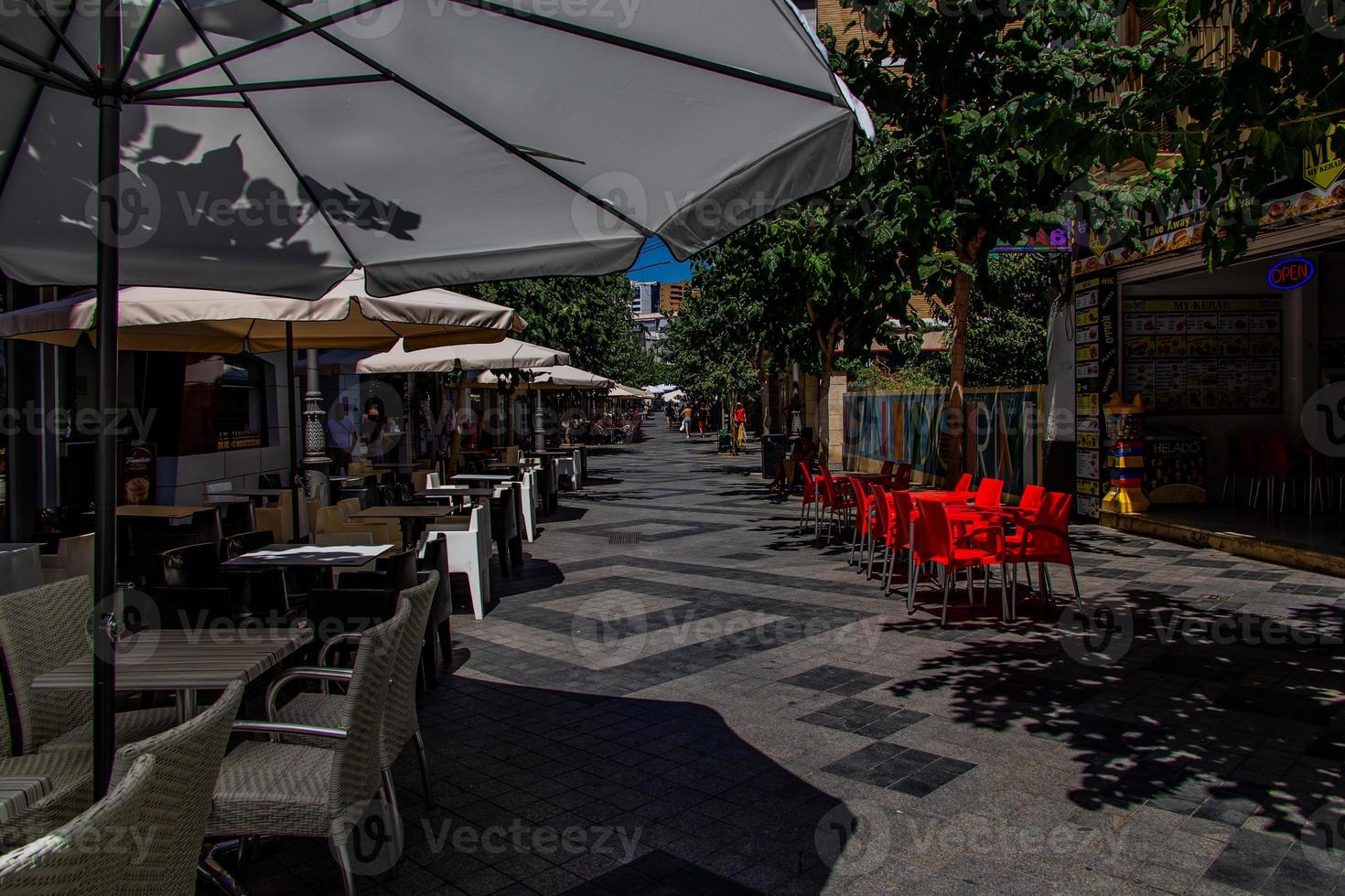 l urban landskap av en spanska gata i benidorm med en Kafé och tabeller på de trottoar utan människor foto