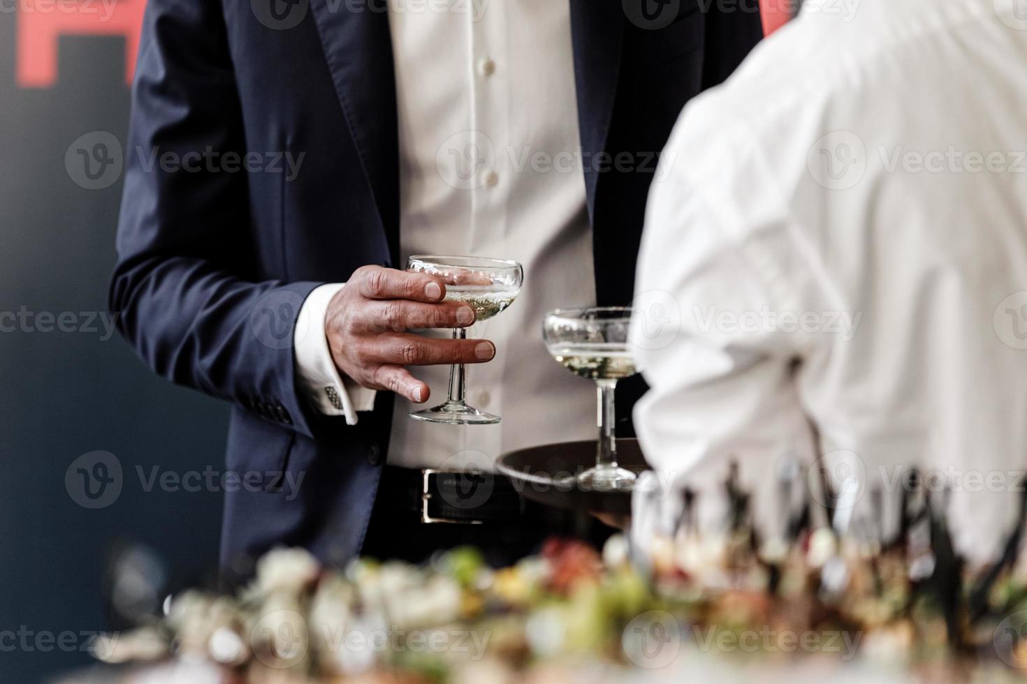 stilig och framgångsrik affärsman i snygg kostym som håller ett glas martini på en fest, företagsfest, konferens, forum, banketter, närbild. selektivt fokus. foto