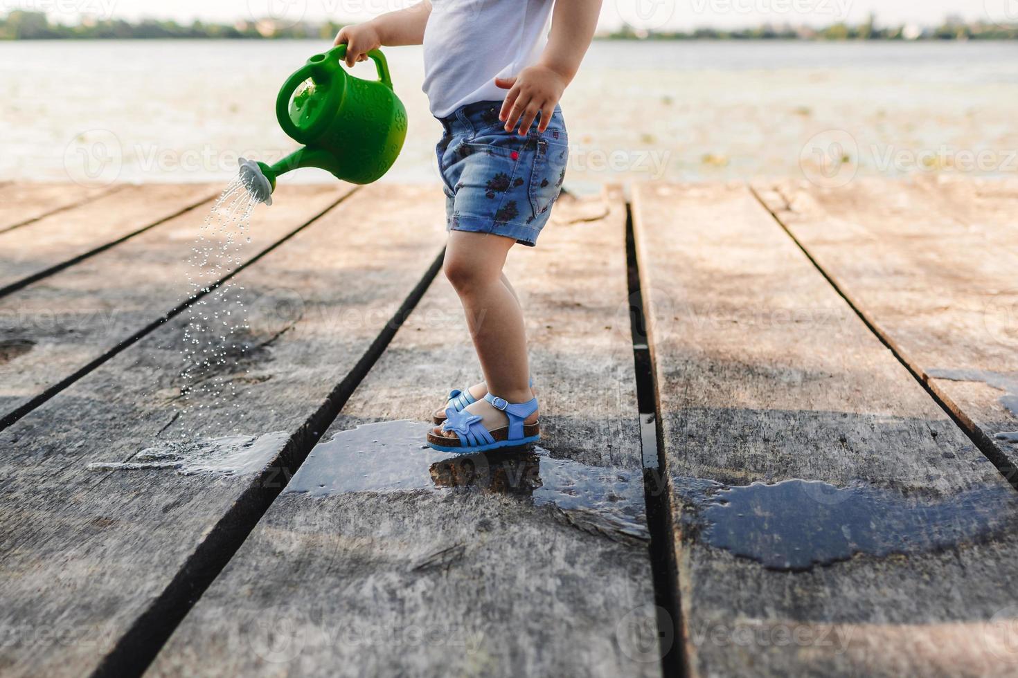 en liten flicka leker med en vattenkanna i en träbro foto