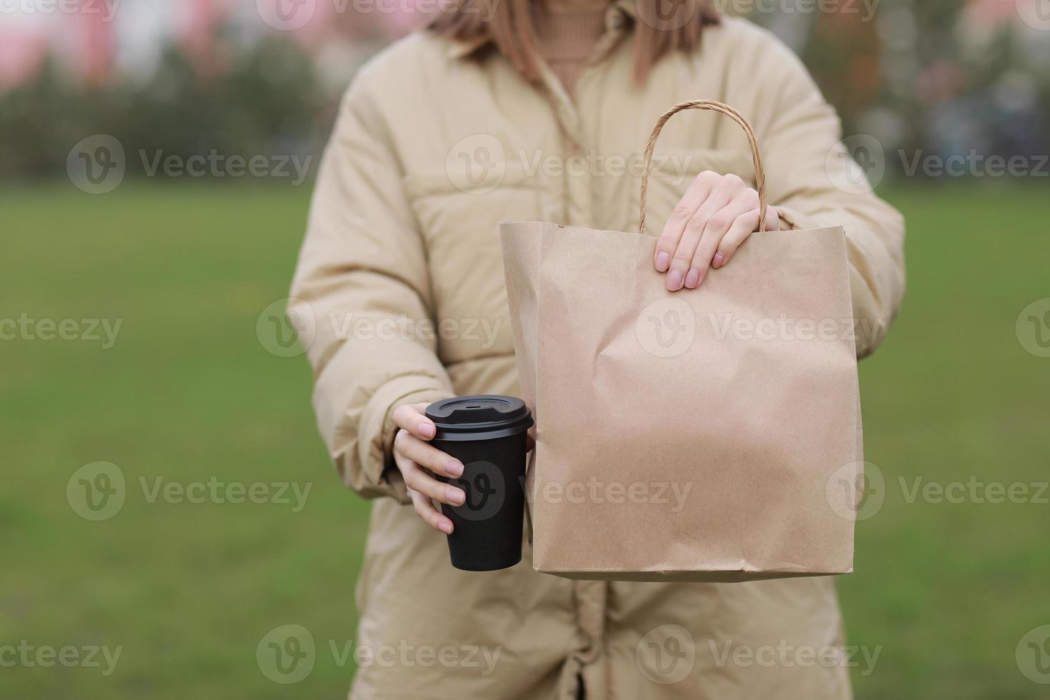 takeaway kopp med kaffe, håna upp för identitetsmärkning. närbild av papperspåse och papperskopp i kvinnlig hand. ung kvinna bär påsar och kaffe foto