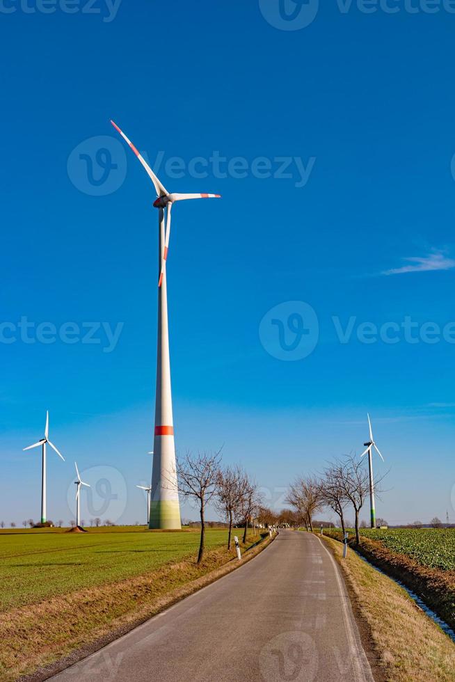 se över skön bruka landskap med tidigt vår lantbruk fält, vind turbiner till producera grön energi och en ensam väg nära mittweida, Tyskland, på blå solig himmel. foto