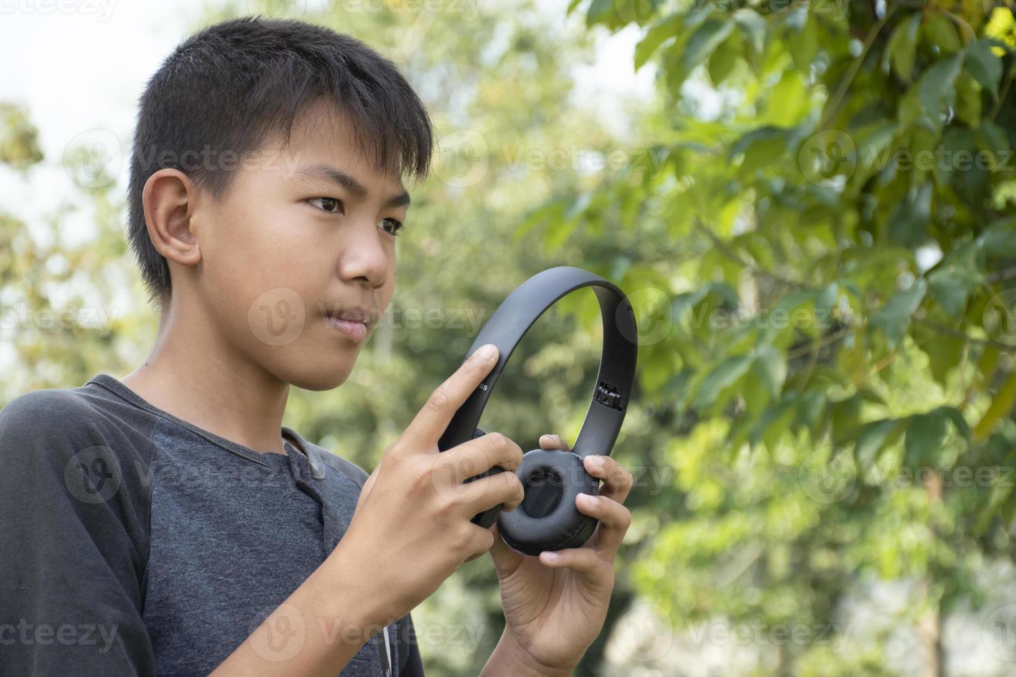 porträtt av asiatisk pojke innehav trådlös hörlur eller hörlurar i de parkera, mjuk och selektiv fokus, lycka och avslappning i dagligen liv av ung människor runt om de värld begrepp. foto