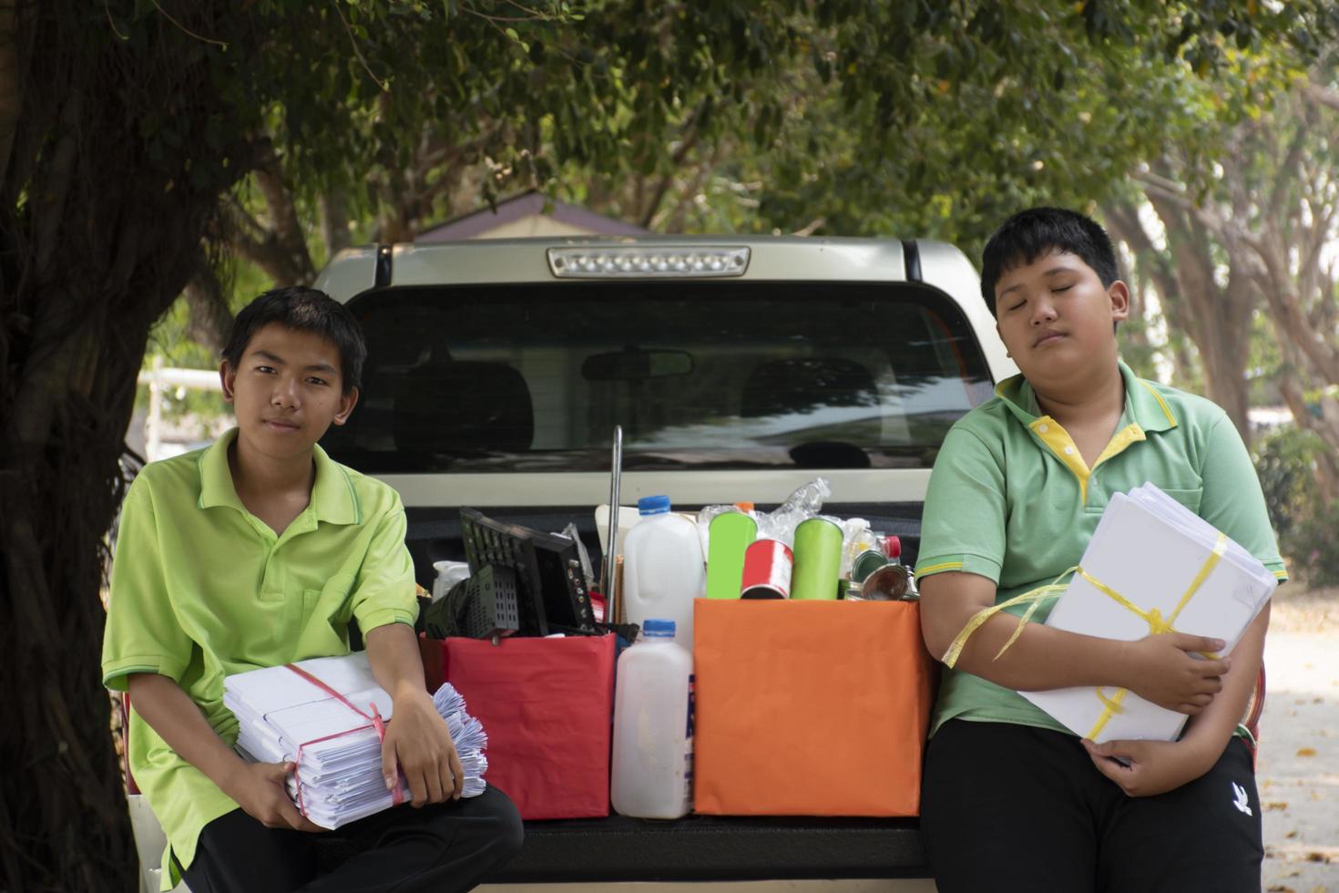 asiatisk pojke i grön t-shirt är separerande annorlunda typer av skräp in i färgkodad lådor i de tillbaka av en plocka upp lastbil innan ledande dem till sälja och generera inkomst efter deras skola högtider. foto